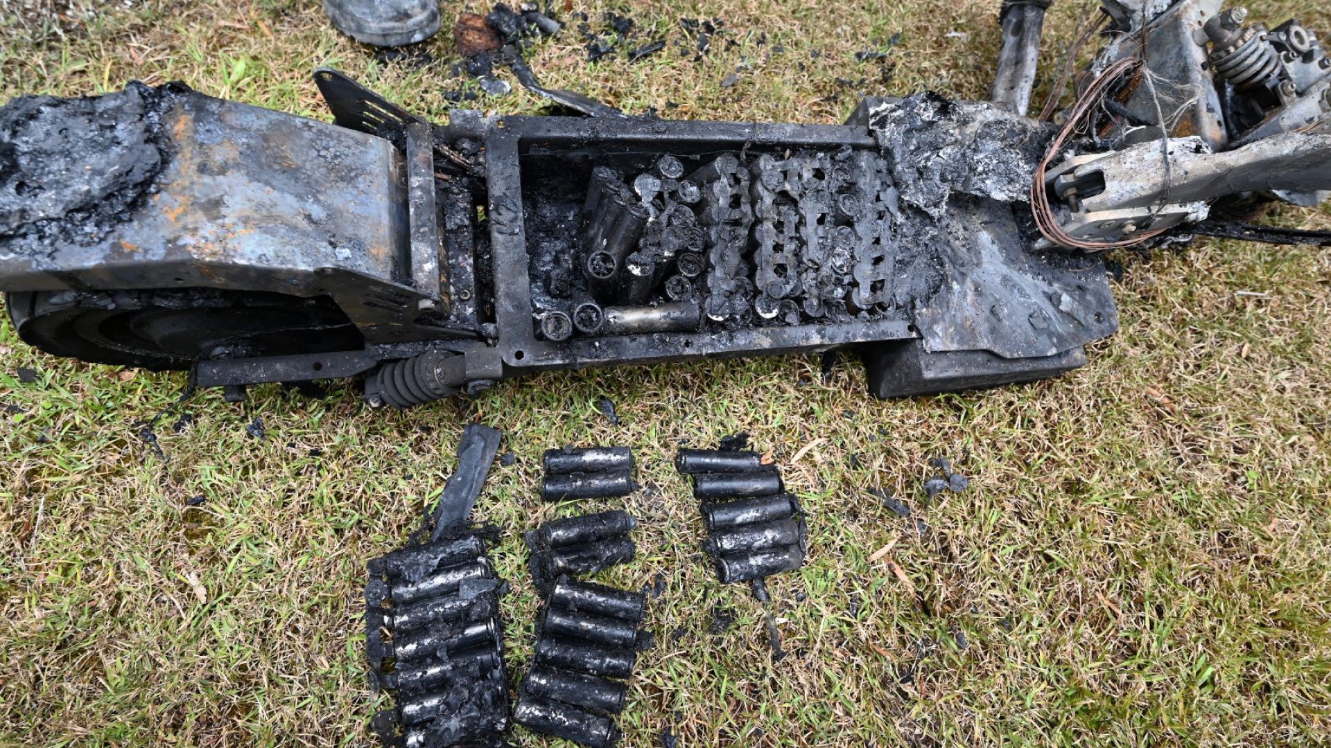 Burnt and charred remnants of a vehicle or machinery on grass