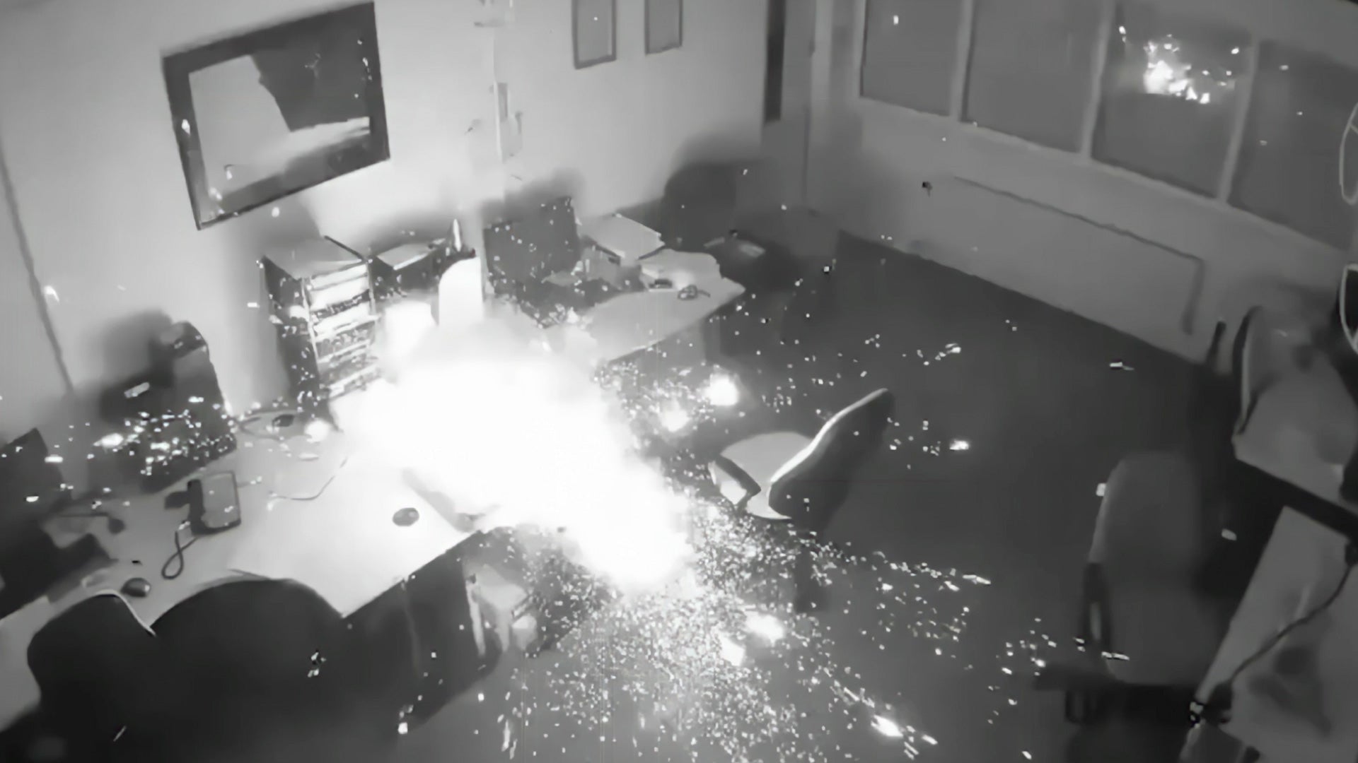 Black and white surveillance footage of a room with a desk and computer equipment.