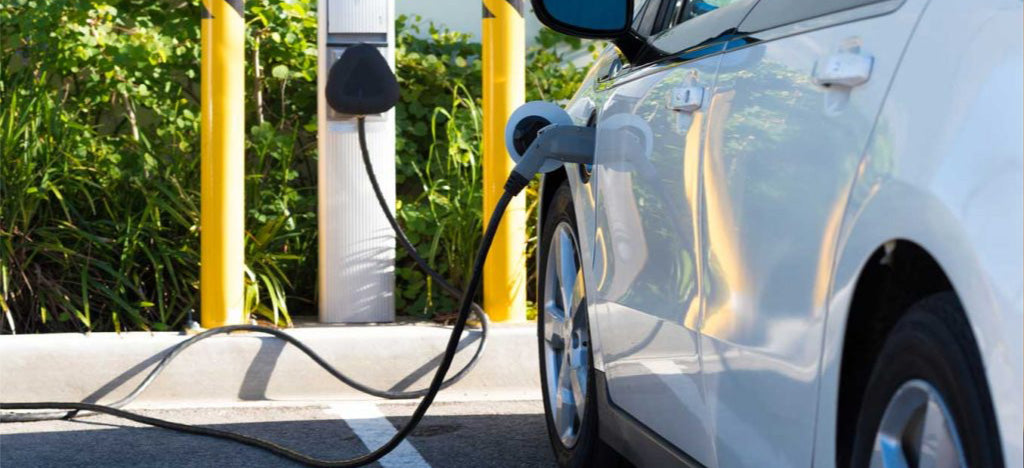 Electric car charging at a charging station with greenery in the background