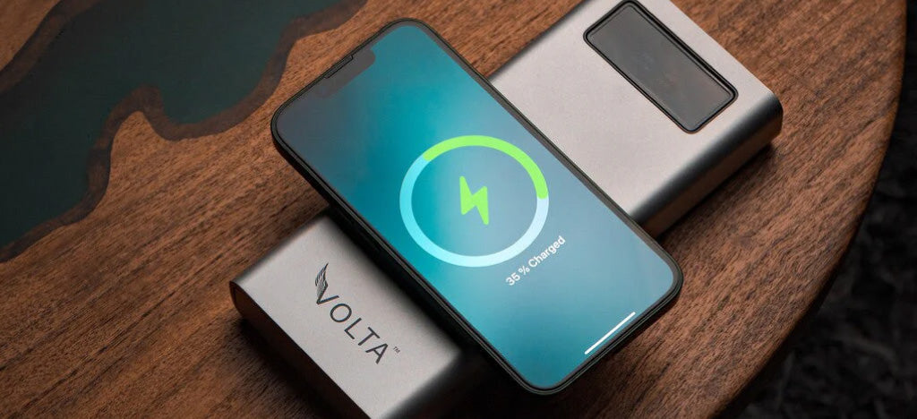 Smartphone with charging icon on screen next to Volta device on wooden surface