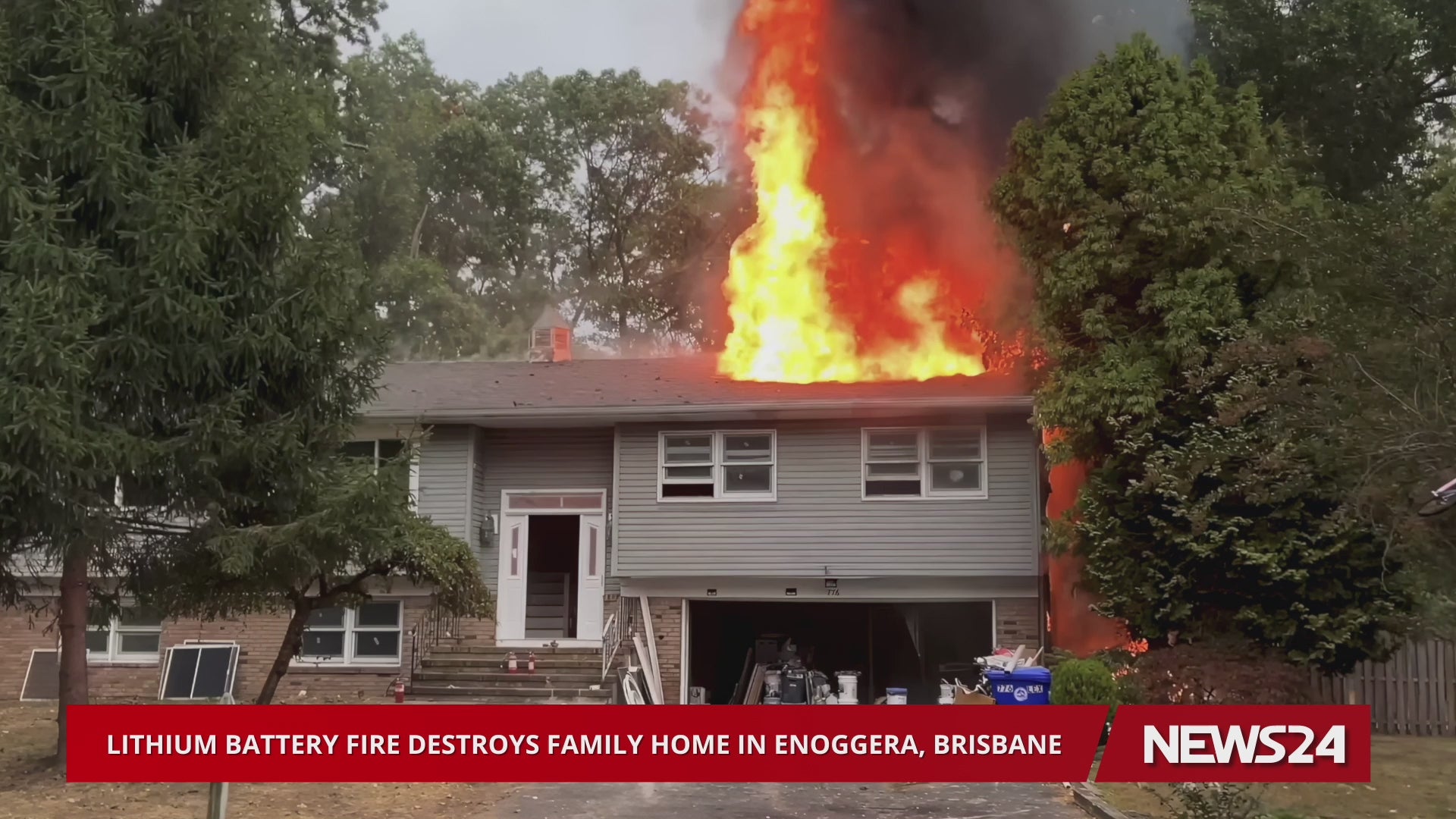 Load video: News report still showing a intense fire erupting from the roof of a suburban home, with a headline reading: 'Lithium Battery Fire Destroys Family Home in Enoggera, Brisbane'.